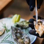 Chef a abrir uma ostra fresca com faca, servida com gelo e limão